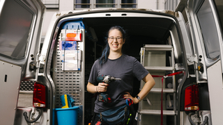 Das Bild zeigt die Kollegin vor ihrem offenen Fahrzeug, mit einem Bohrer in der Hand.