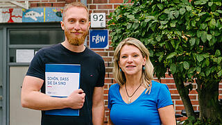 Zwei Mitarbeitende nebeneinander vor einem Haus